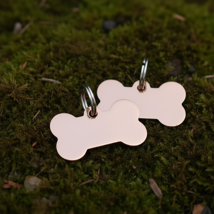 Two bone-shaped rose gold pet tags on a green moss background