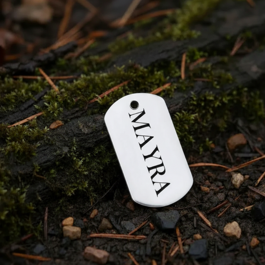 Silver dog tag with 'MAYRA' engraved on a mossy log