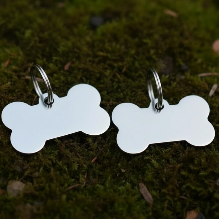 Two bone-shaped silver pet tags on a mossy background