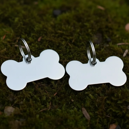 Two bone-shaped silver pet tags on a mossy background