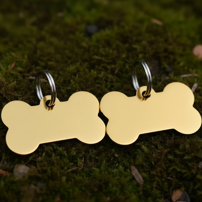 Two gold bone-shaped dog tags on a green moss background